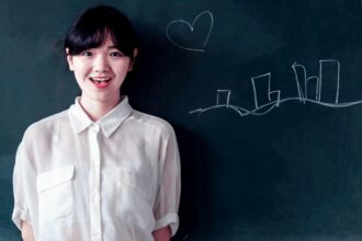 Smiling young woman stands confidently by a blackboard with chalk drawings.